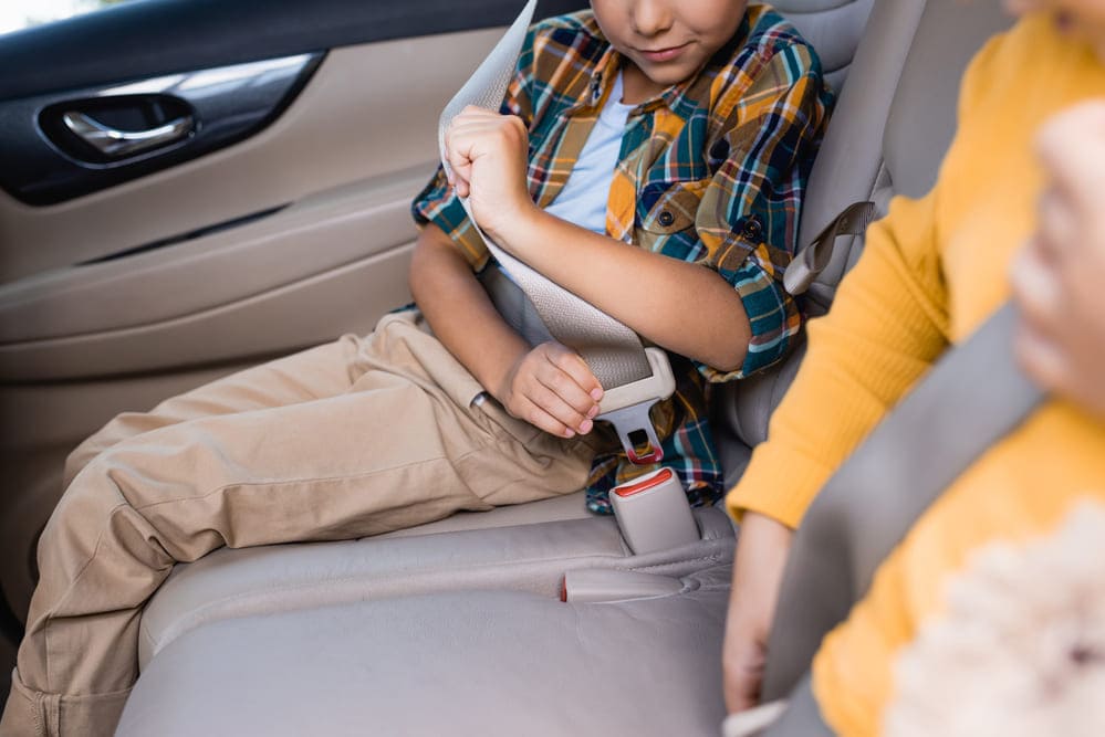 kid sitting on backseat adjusting seatbelt