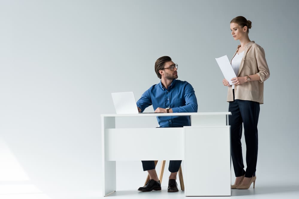 man sitting at desk watching at woman standing