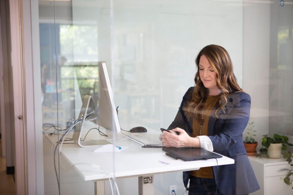 woman standing at standing desk with mobile phone in hand